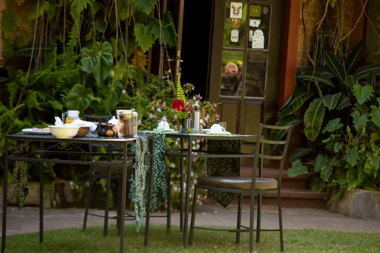 A breakfast table laid in the lodge garden at Mullers, framed by lush greenery beside the main-house doors