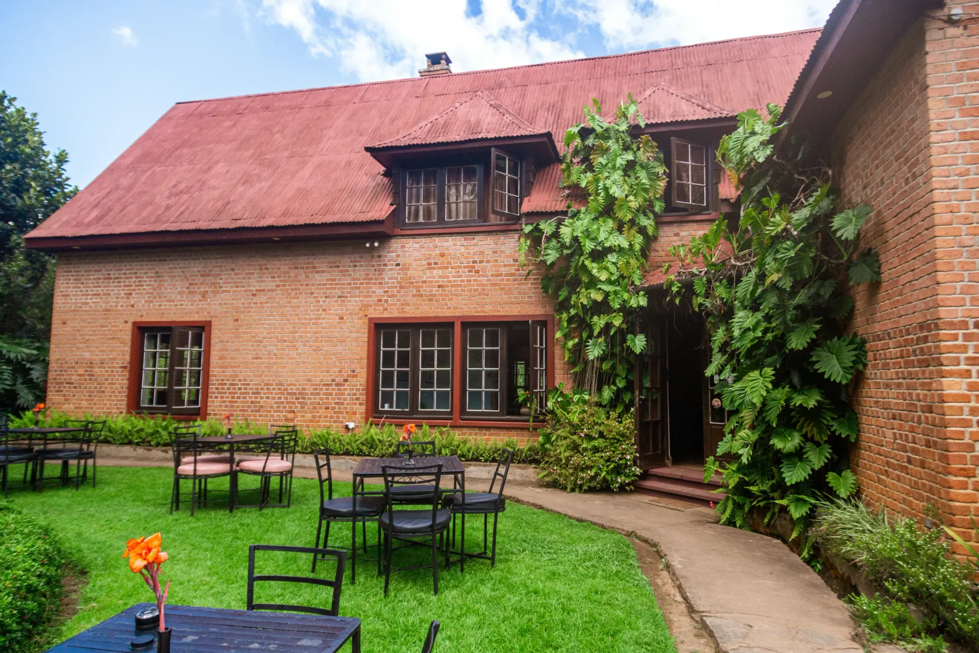 The back of the brick farmhouse, ivy climbing the entrance, with café tables set on the garden lawn