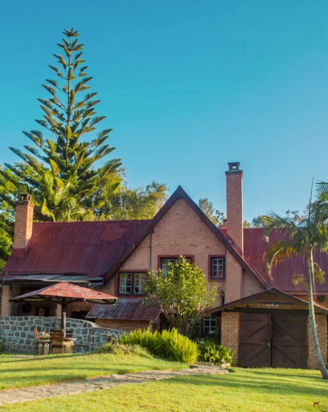 The brick farmhouse at Mullers, its red roof and chimney rising above a stone wall banked with orange and purple hydrangeas